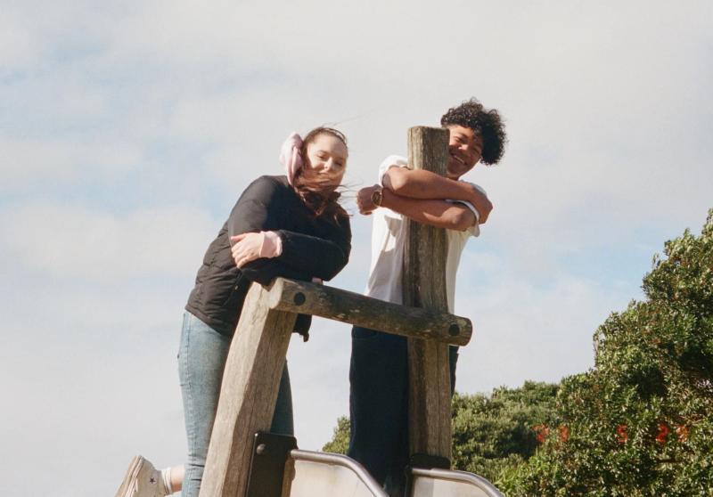 a man and a woman leaning on a wooden post