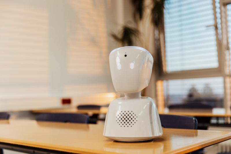 A small white AV1 robot sits on a wooden table.
