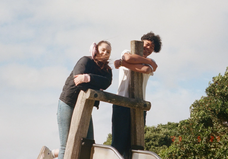a man and a woman leaning on a wooden post
