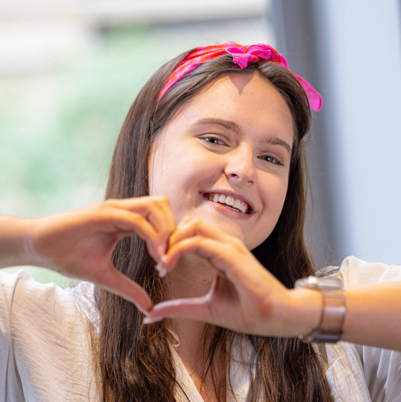a woman wearing a pink headband makes a heart shape with her hands a woman wearing a pink headband makes a heart shape with her hands