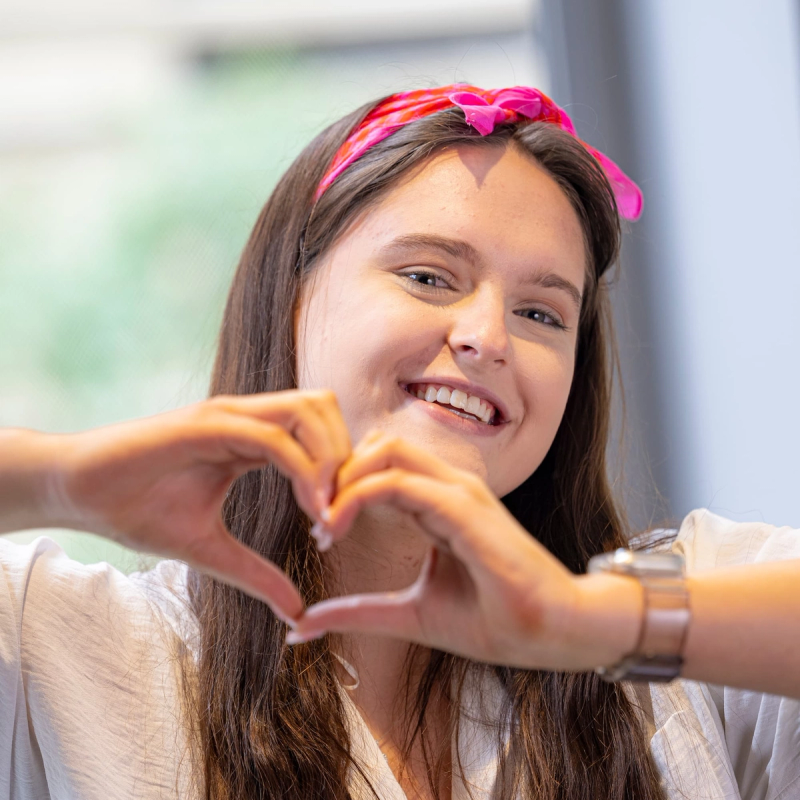 a woman wearing a pink headband makes a heart shape with her hands