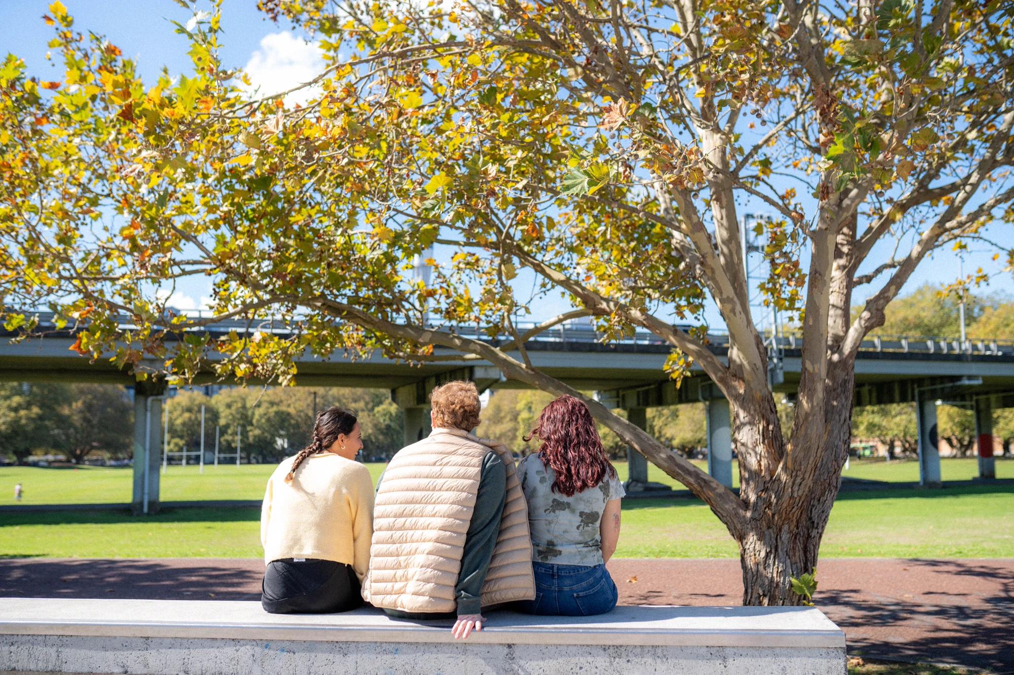 three young people sitting on a bench and talking.