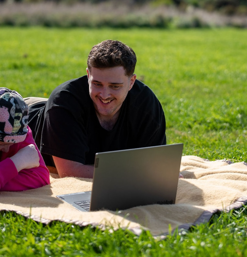 a man and a girl laying on a blanket looking at a laptop