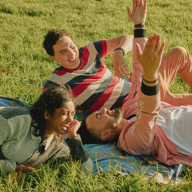 three people are laying on a blanket in the grass and one of them is wearing a shirt that says ' pink ' on it