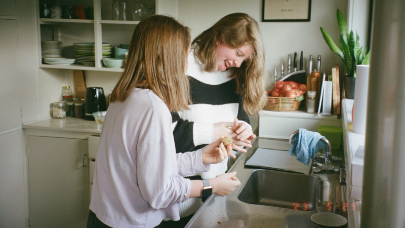 two girls are laughing in a kitchen with a picture on the wall that says ' i love you '
