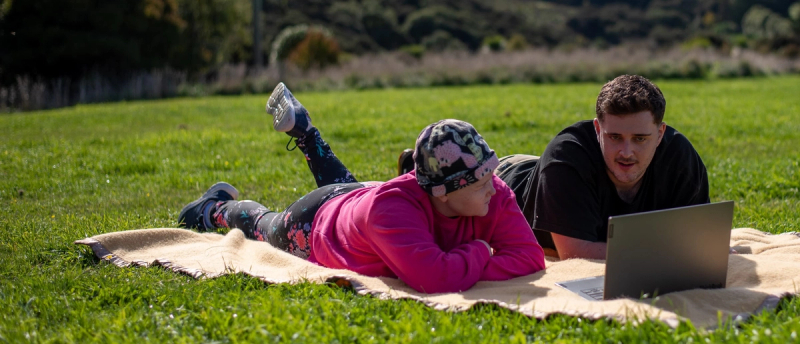 a man and a woman laying on a blanket with a laptop