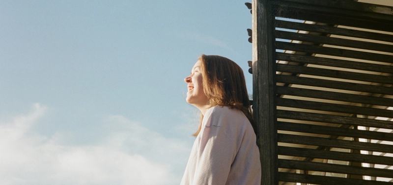 a woman leaning against a wooden fence looking up at the sky