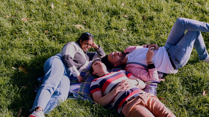 three people laying on a blanket in the grass