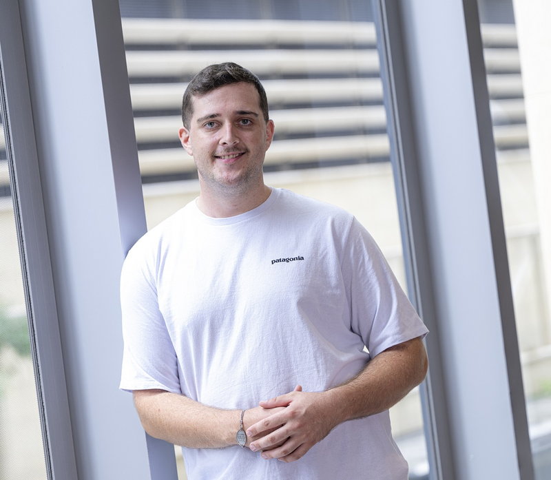 a man wearing a white patagonia shirt stands in front of a window