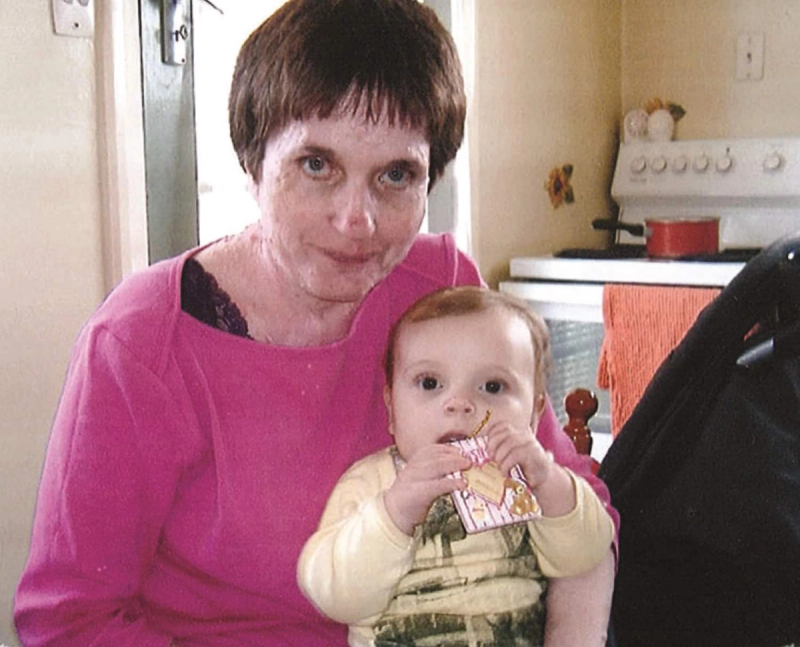 a woman in a pink shirt is holding a baby in front of a stove