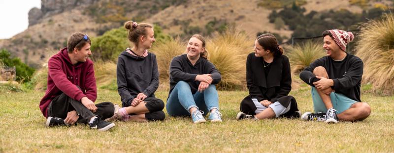 a group of people sitting on the grass with one wearing a hat that says ' supreme ' on it