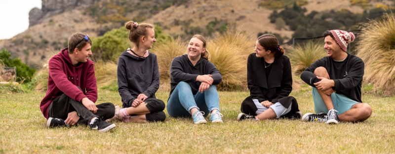 a group of people sitting on the grass with one wearing a hat that says ' supreme ' on it a group of people sitting on the grass with one wearing a hat that says ' supreme ' on it