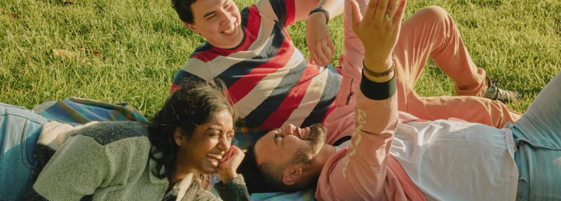 a group of people are laying on a blanket in the grass . a group of people are laying on a blanket in the grass .