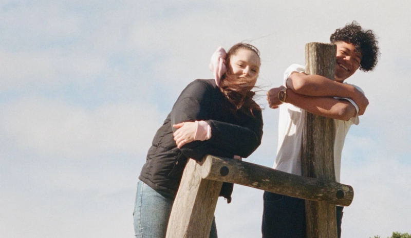 a man and a woman leaning on a wooden post