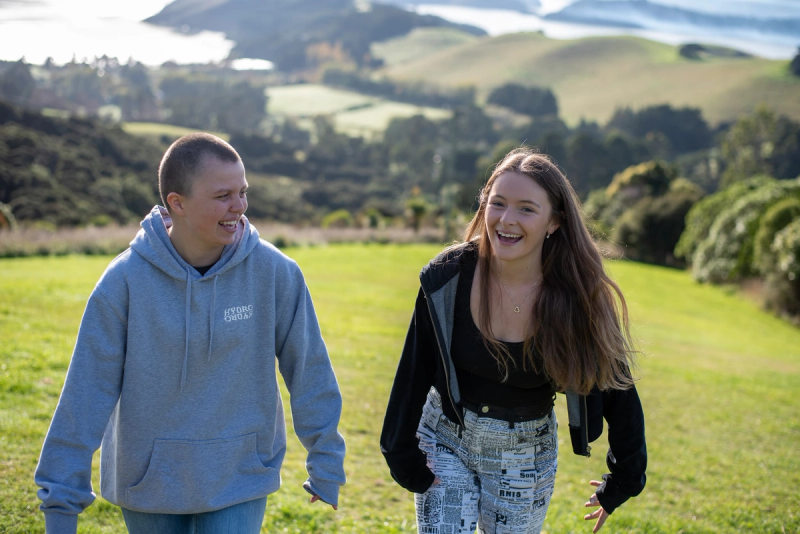 a boy and a girl are walking in a grassy field and the boy is wearing a hoodie that says auckland a boy and a girl are walking in a grassy field and the boy is wearing a hoodie that says auckland