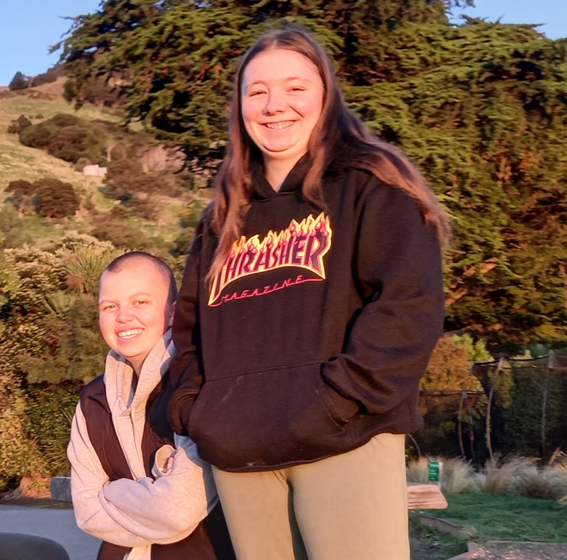 a girl wearing a thrasher hoodie stands next to another girl