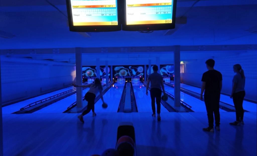 Bowlare i UV-ljus: en spelare släpper klotet medan kompisarna tittar på