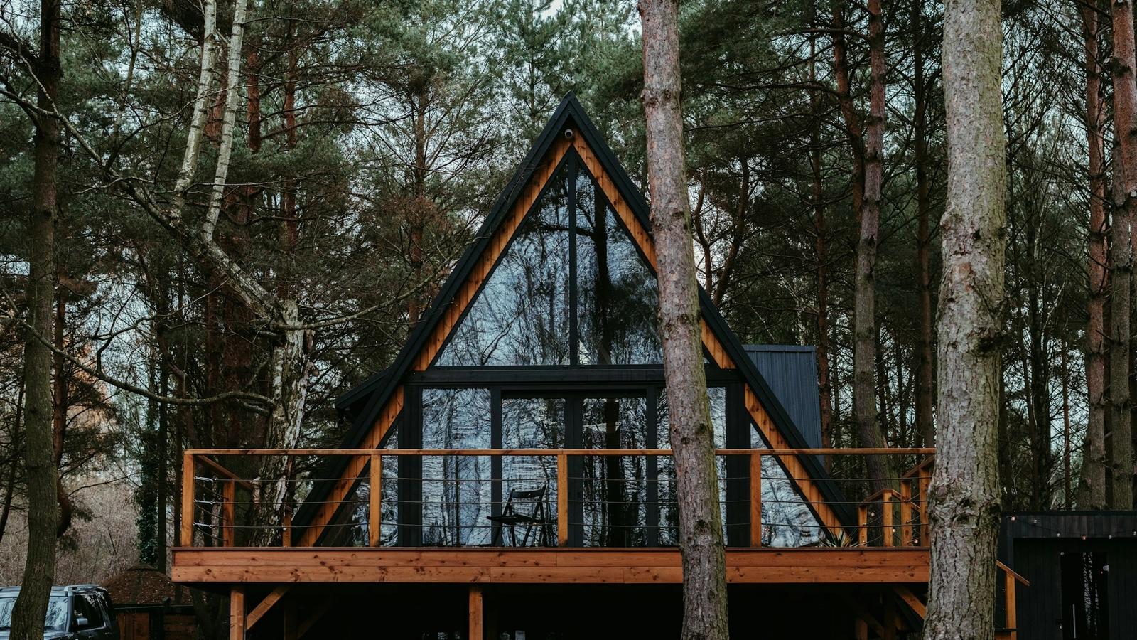 A glass-fronted A-frame cabin with a timber deck, set among tall trees