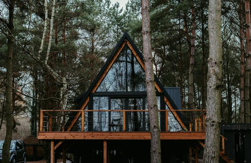 A glass-fronted A-frame cabin with a timber deck, set among tall trees
