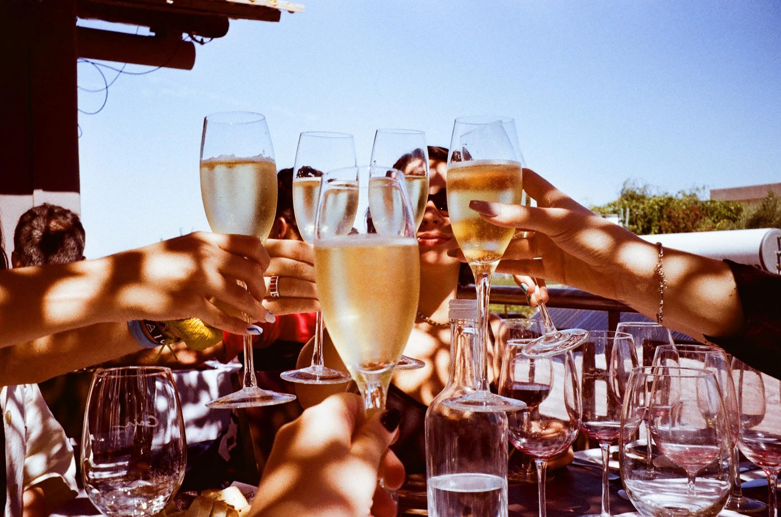 An image of people joining together glasses of sparkling white wine while celebrating.