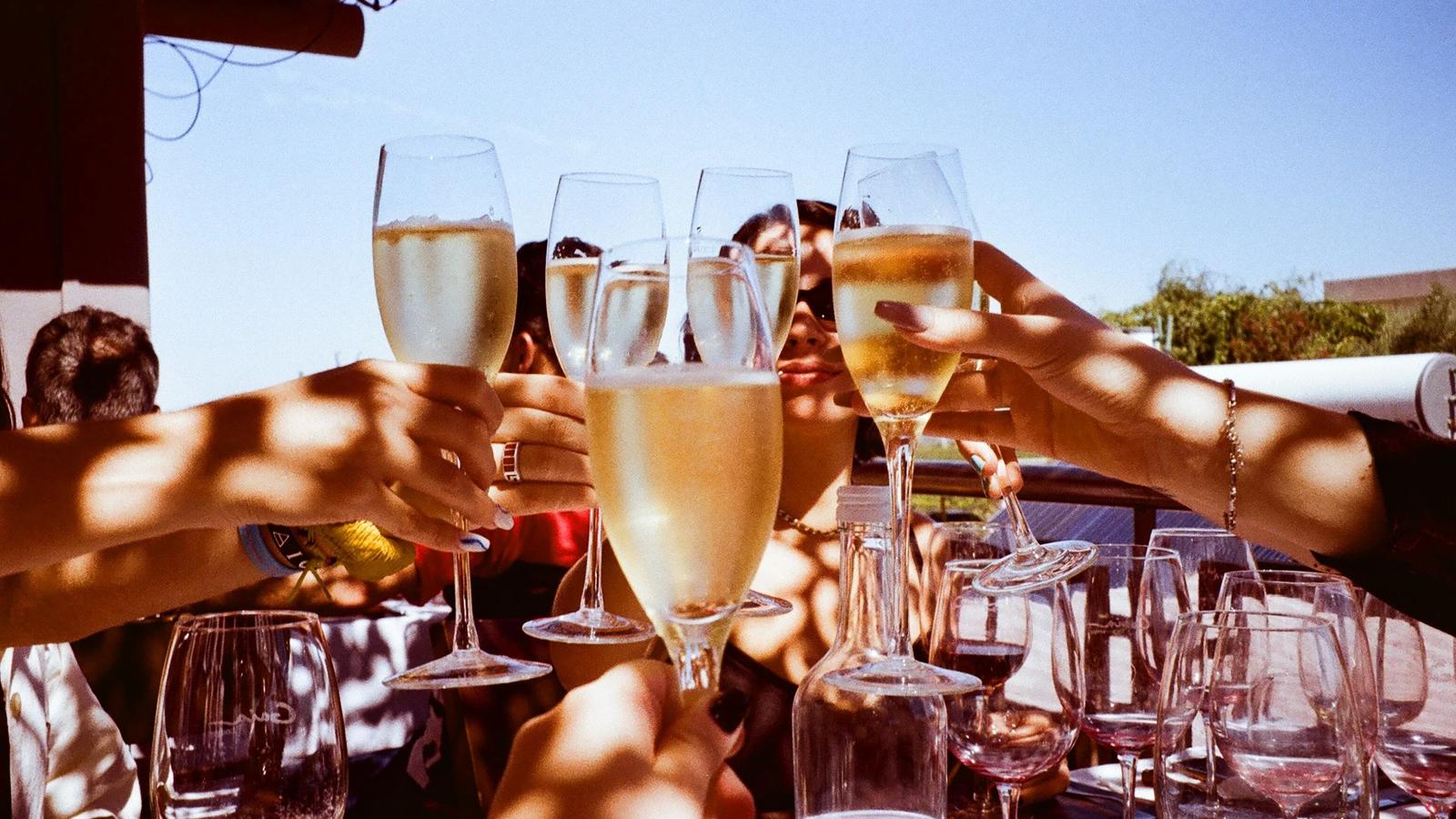 An image of people joining together glasses of sparkling white wine while celebrating.
