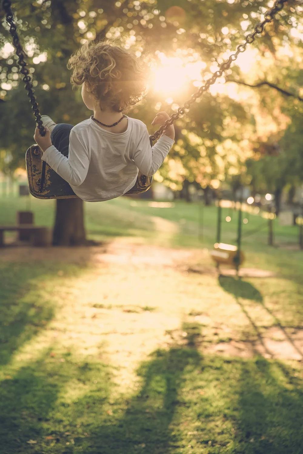 A child wearing a white shirt playing on a swing at a winery at sunset. 