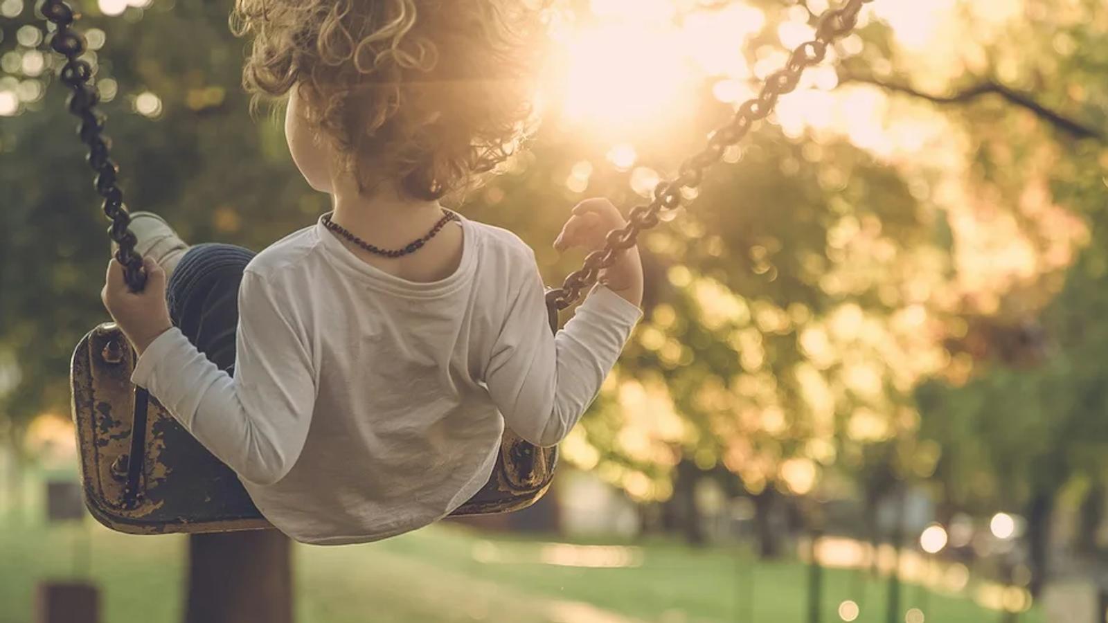 A child wearing a white shirt playing on a swing at a winery at sunset.