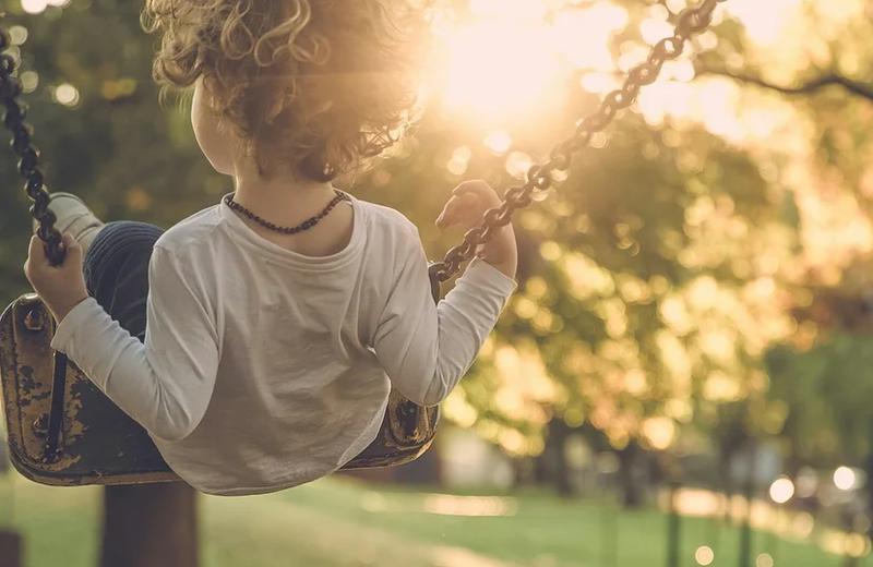 A child wearing a white shirt playing on a swing at a winery at sunset.