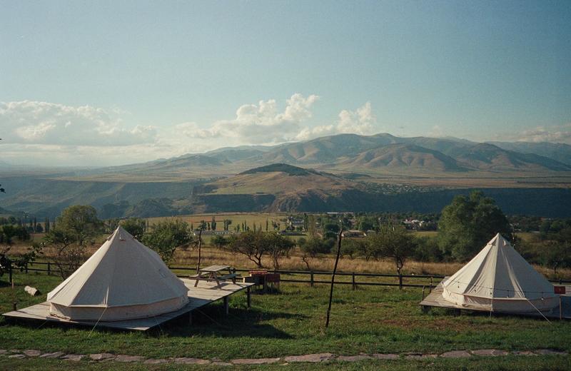 Two white canvas bell tents on timber platforms in a grassy field, with hills in the distance