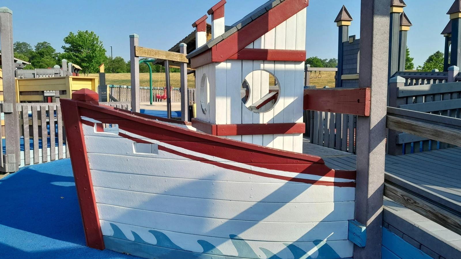 A boat shaped timber play structure in a playground under a clear blue sky.