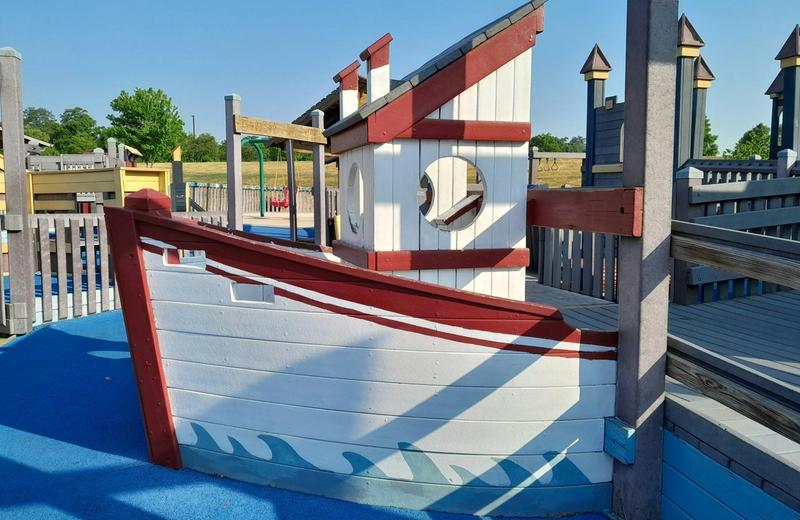 A boat shaped timber play structure in a playground under a clear blue sky.