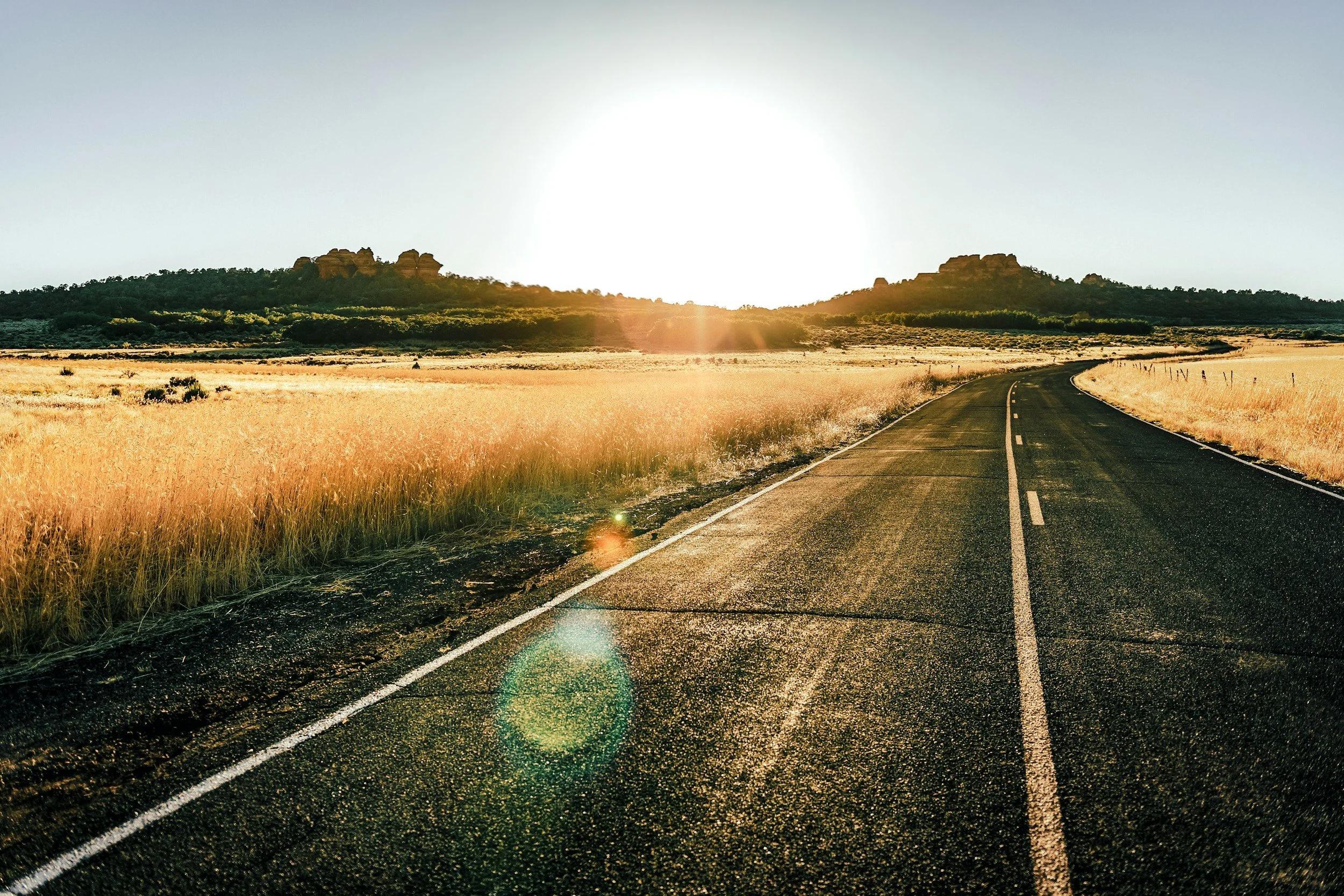 An image of a long winding road at sunset with fields of brown grasses on either side. 