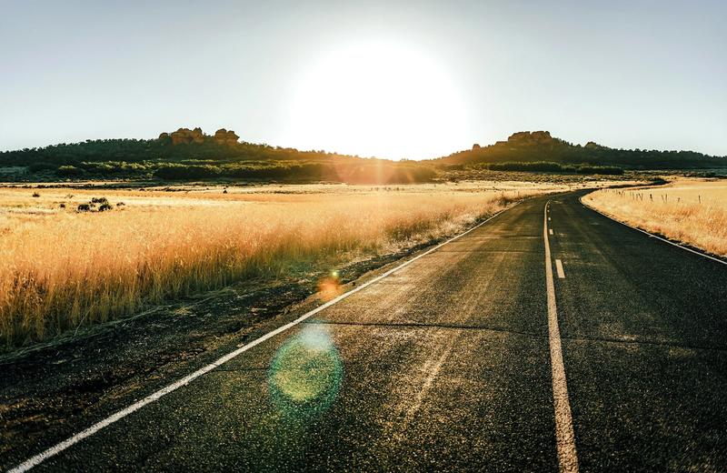 An image of a long winding road at sunset with fields of brown grasses on either side.