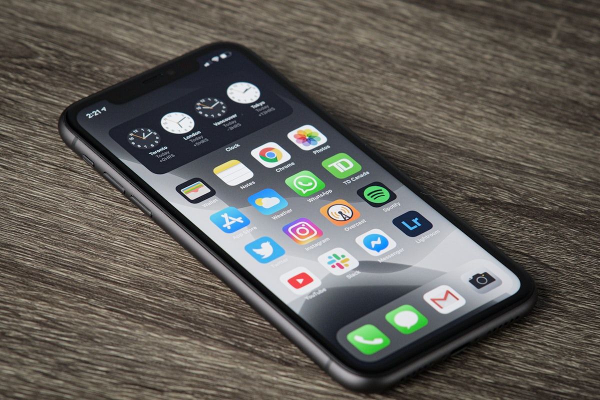 Un smartphone posé sur un plan de travail en bois, écran d’accueil rempli d’icônes d’applications.