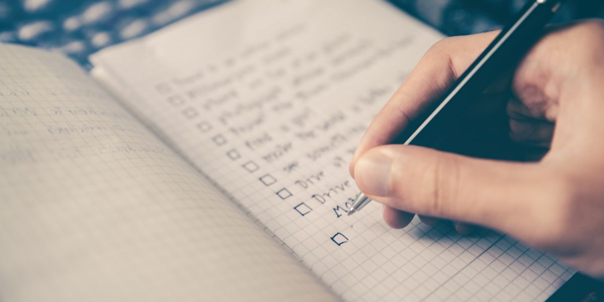 A hand writing a list in pencil in a squared notebook.