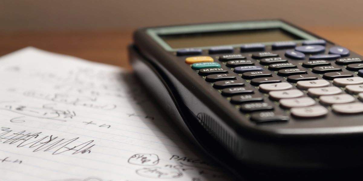 A scientific calculator resting on a sheet covered in handwritten calculations.