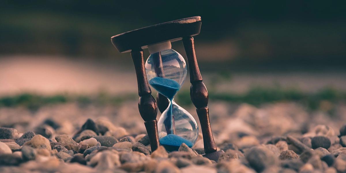 An hourglass standing on pebbles, its sand running through.