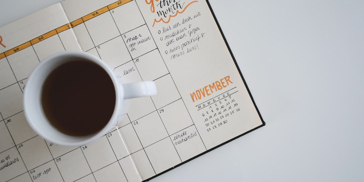 A cup of coffee sitting on an open monthly planner.