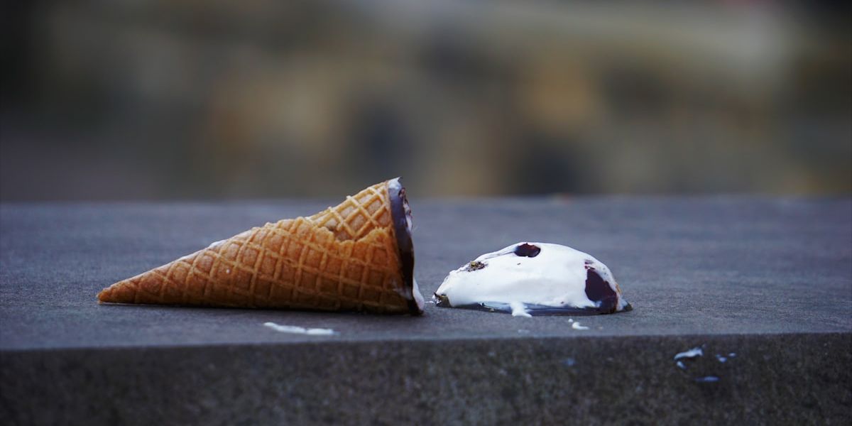 A dropped ice cream, the cone tipped over on the pavement.