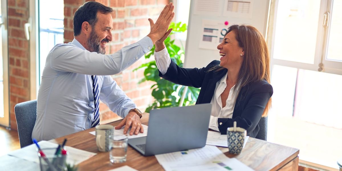 Two people high-fiving over a desk, an open laptop in front of them.