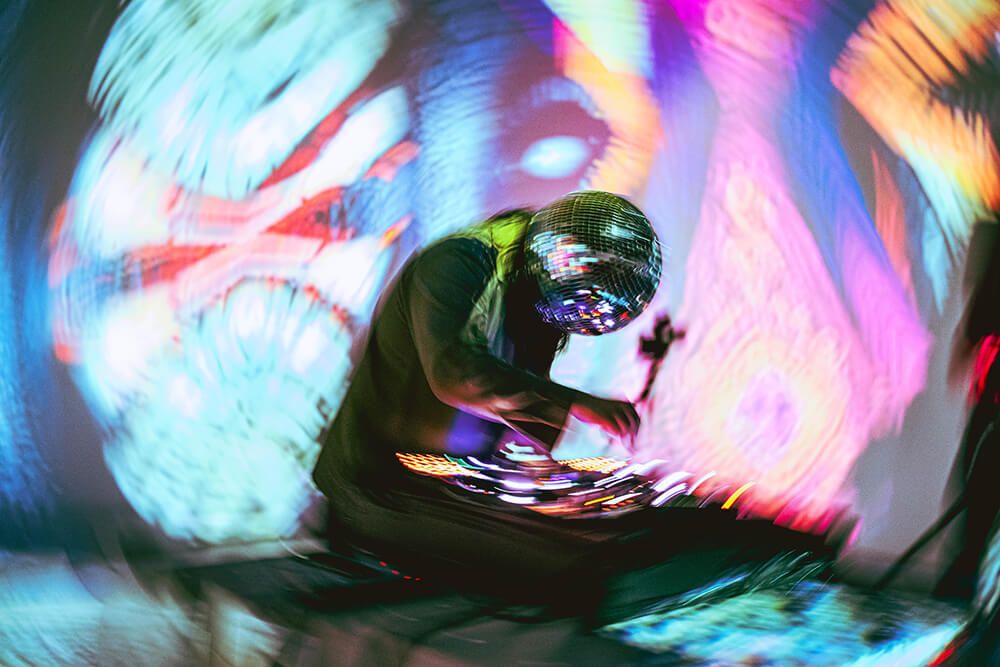 Performer wearing a mirrored helmet surrounded by projected colour