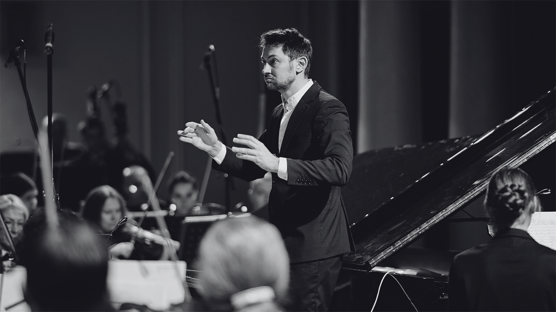 A classical orchestra, with the conductor, on stage performing.