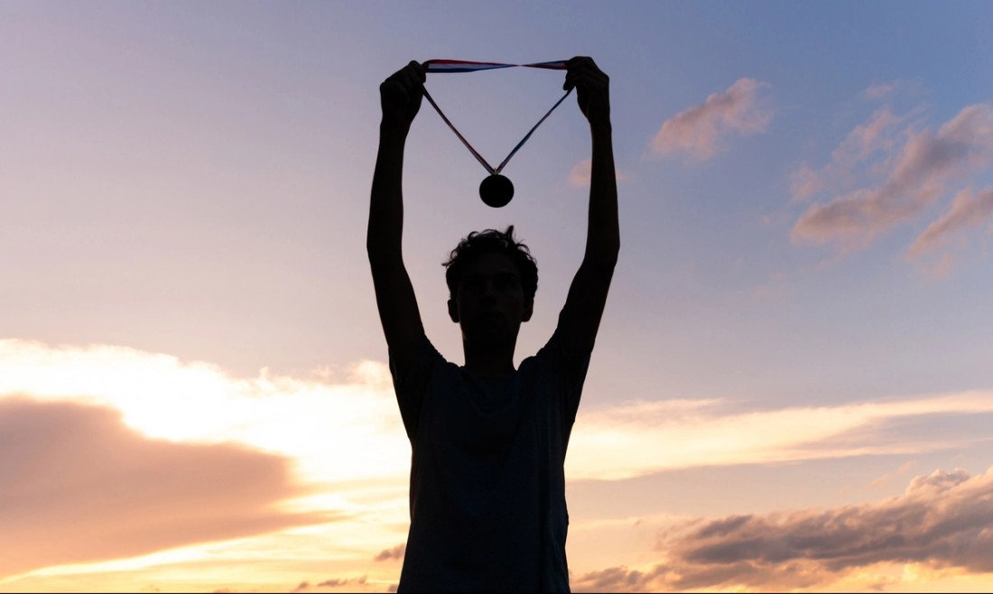 Athlete holding up sports medal in front of sunset
