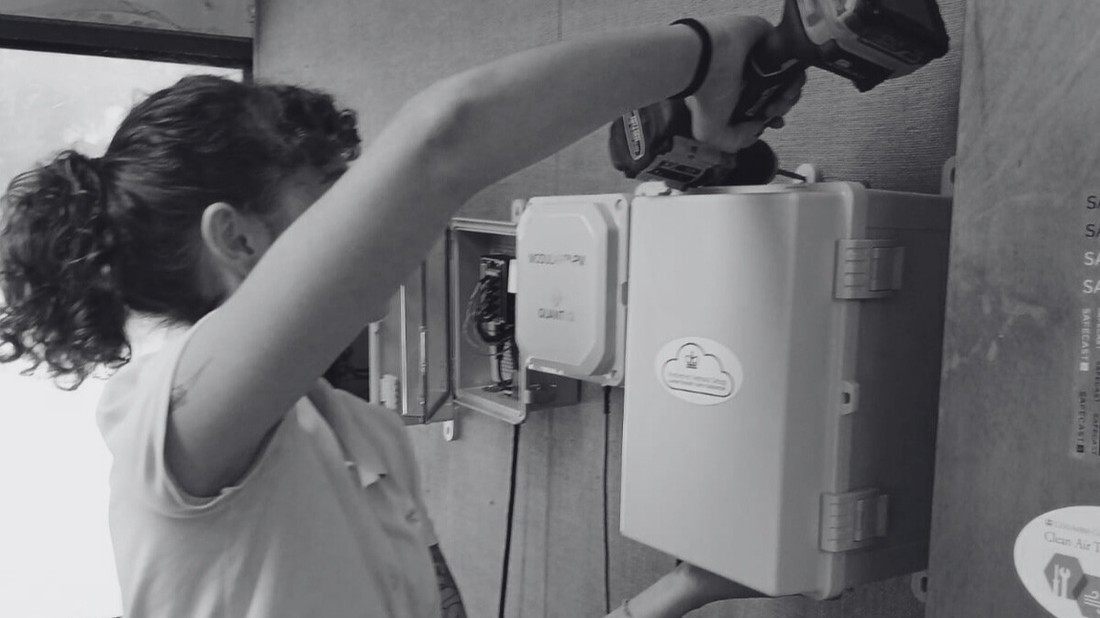 Woman using an electric drill on an air monitoring device.