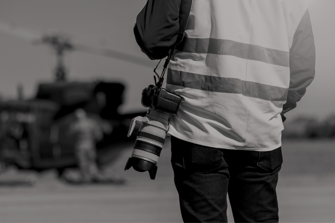 A journalist stands with a camera at their side.