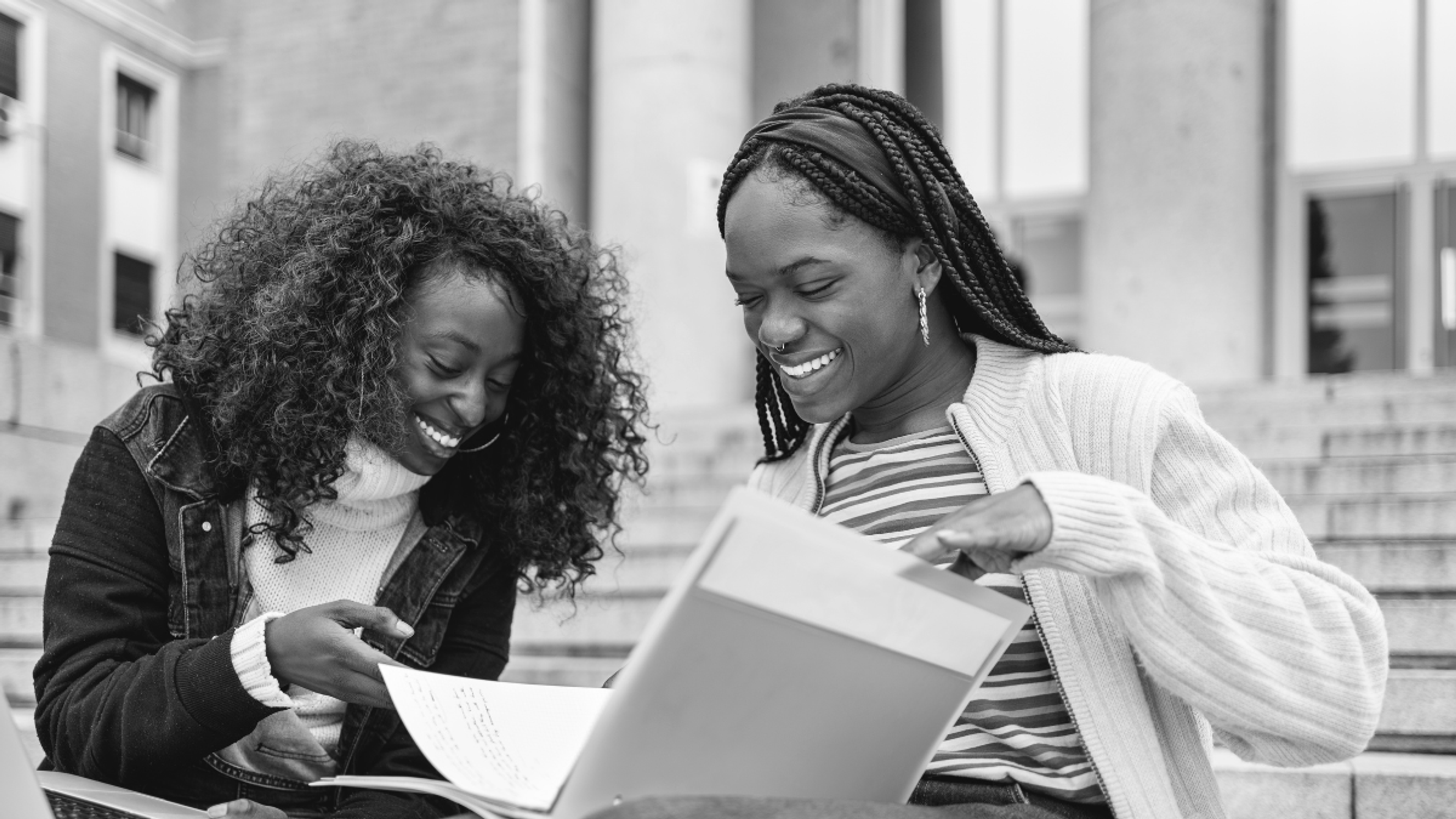 A student looks at a binder with a teacher, both laughing.