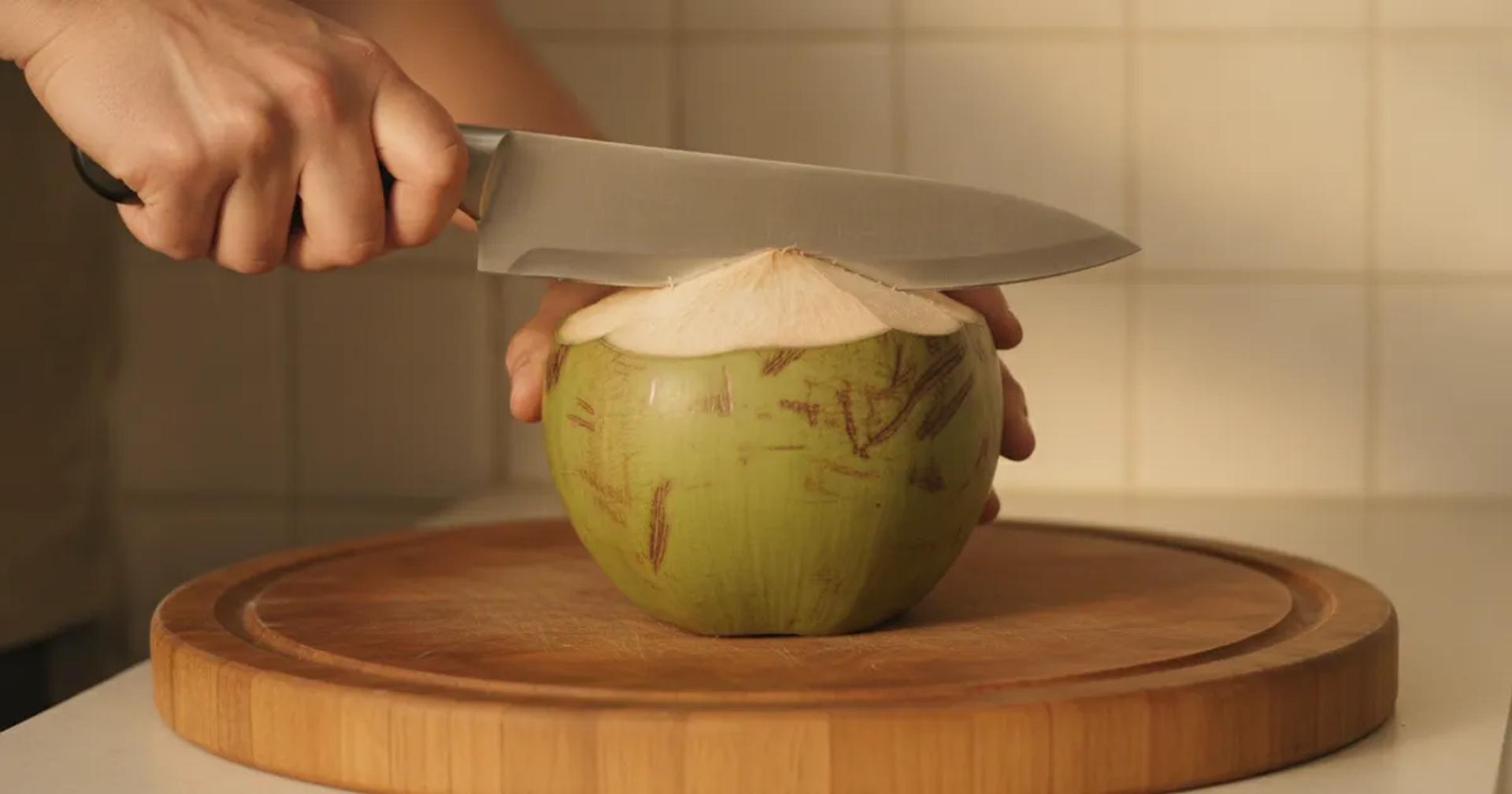 ידיים פותחות קוקוס ירוק טרי עם מקצוע על דלפק מטבח ביתי
