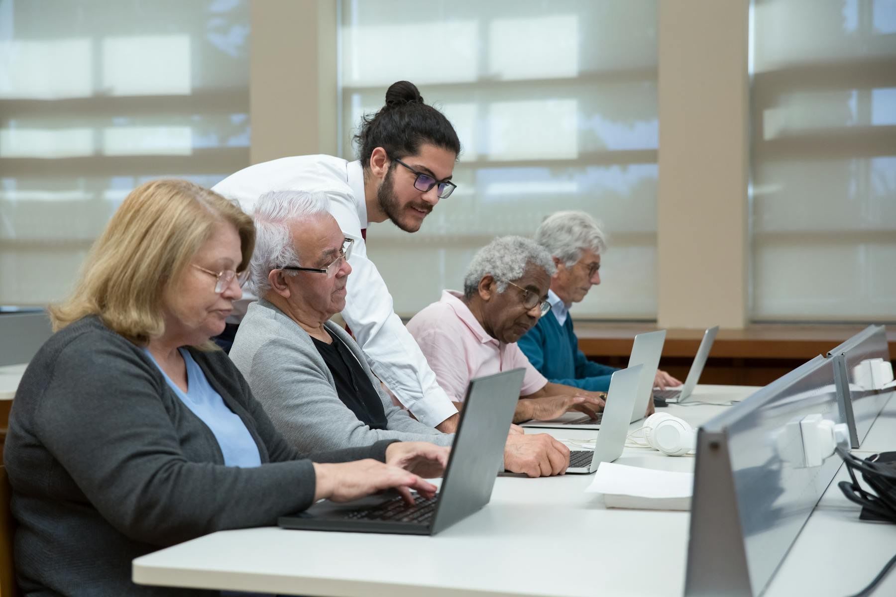 An instructor helps a group of older adults learn to use laptops in a class.