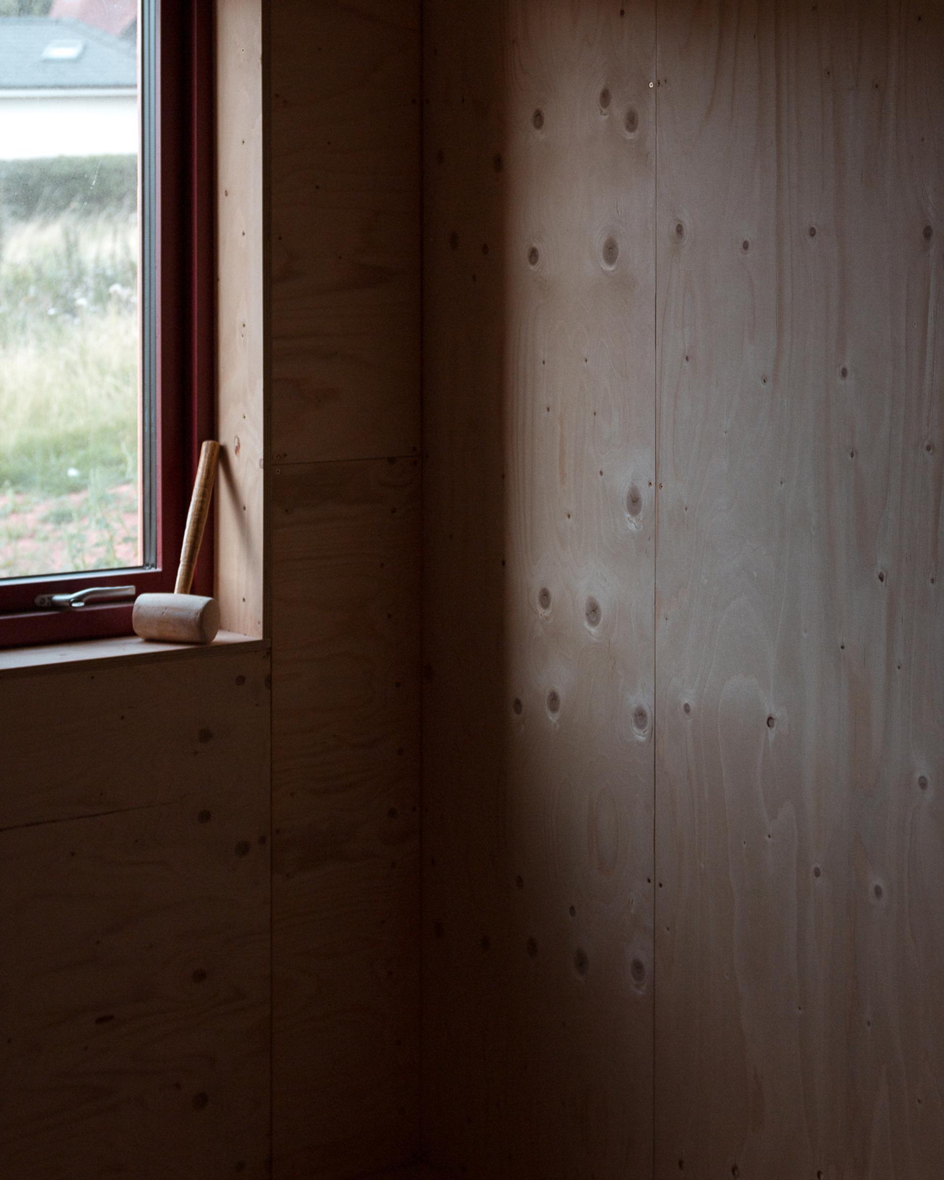 A wooden mallet, upcycled and full of character, rests on the windowsill of a room with unfinished wooden walls. Soft natural light comes through the window, highlighting the wood grain and texture.