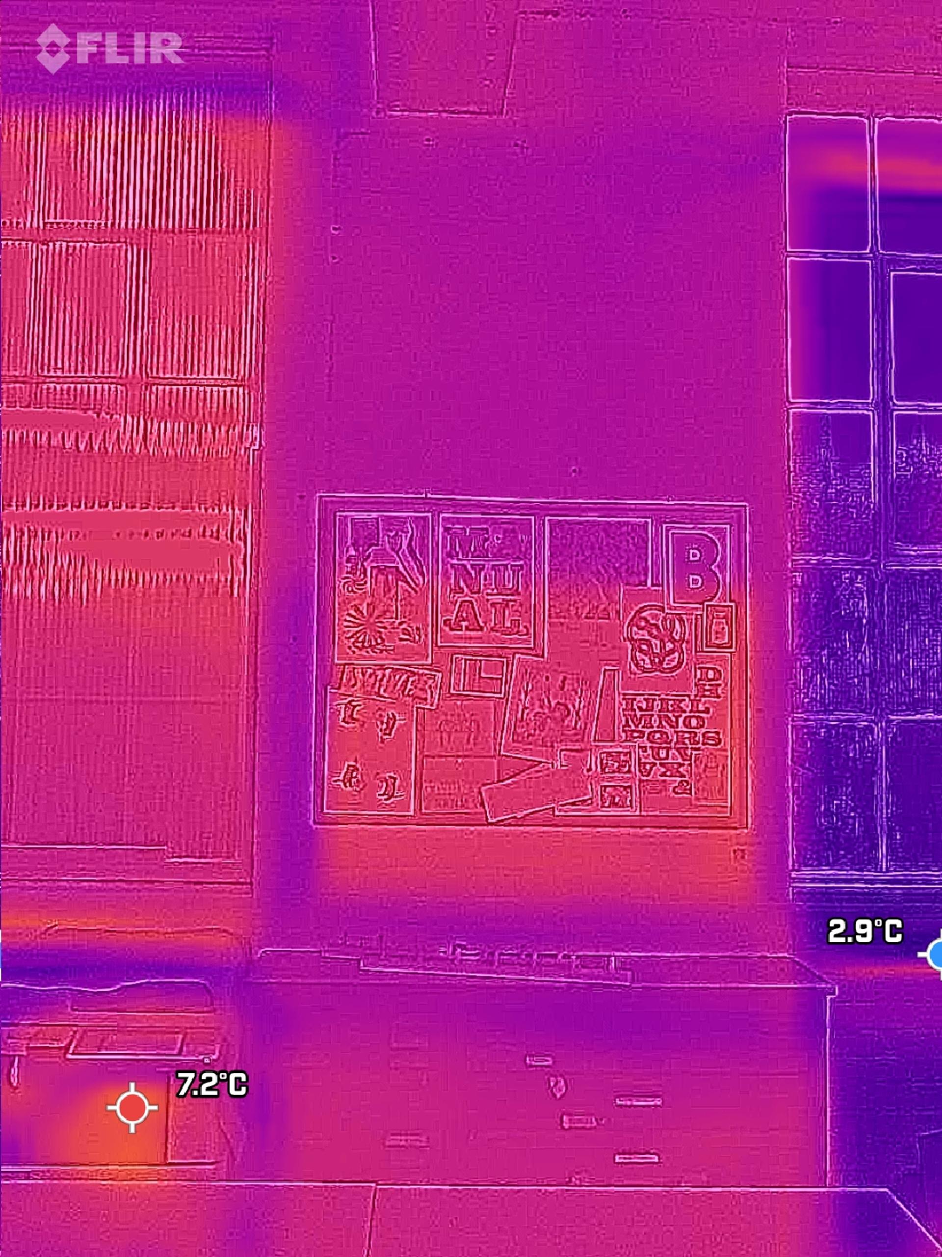 Thermal image showing a wall with a collage of posters in the centre, a warmer modular rectangular area on the left, and cooler objects below—possibly spruce or plywood; temperature readings show 7.2°C (bottom left) and 2.9°C (bottom right).